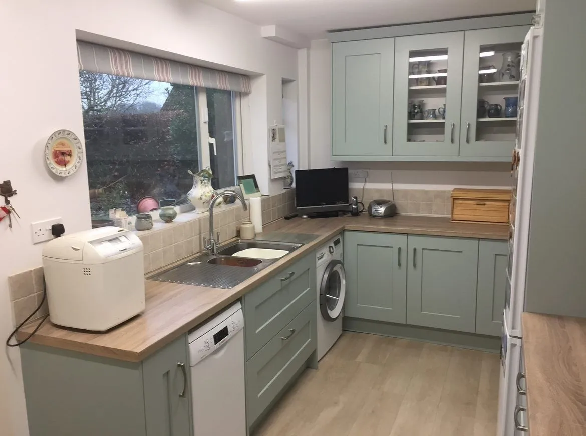 Sage green shaker kitchen in Oxford with sink under the window and wood-effect worktops, fitted by Kitchenroom